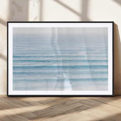 Minimalist ocean view with soft blue waves and a lone surfer, creating a serene and airy coastal aesthetic, perfect for tranquil home decor.