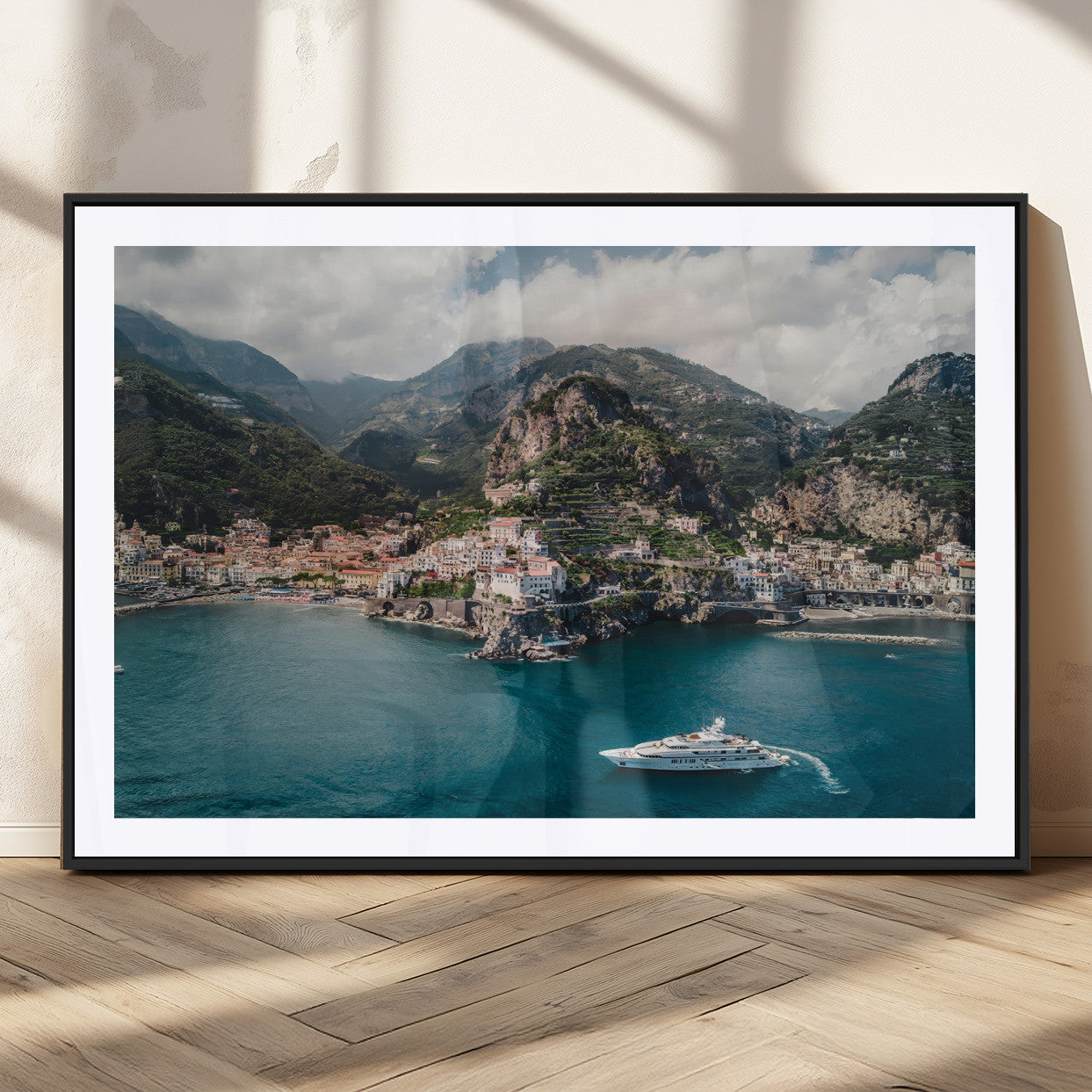 Aerial view of Amalfi Coast, Italy, with colorful hillside houses, lush green mountains, and a luxury yacht sailing in turquoise waters.
