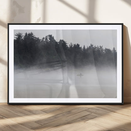 A lone surfer carrying a board through a misty shoreline, surrounded by dense trees and fog, creating a peaceful and mysterious coastal scene.