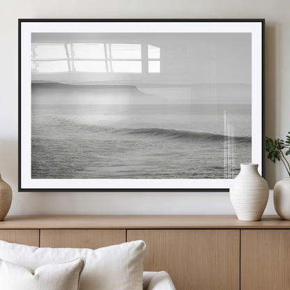 A black and white minimalist seascape featuring soft rolling waves and misty distant cliffs, creating a serene and timeless coastal atmosphere.
