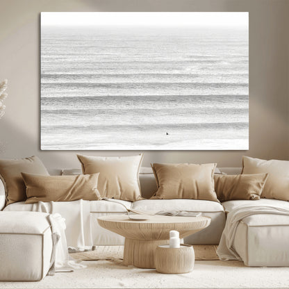 Monochrome photo of a lone surfer in calm layered waves, perfect for minimalist coastal or moody ocean-inspired wall decoration.