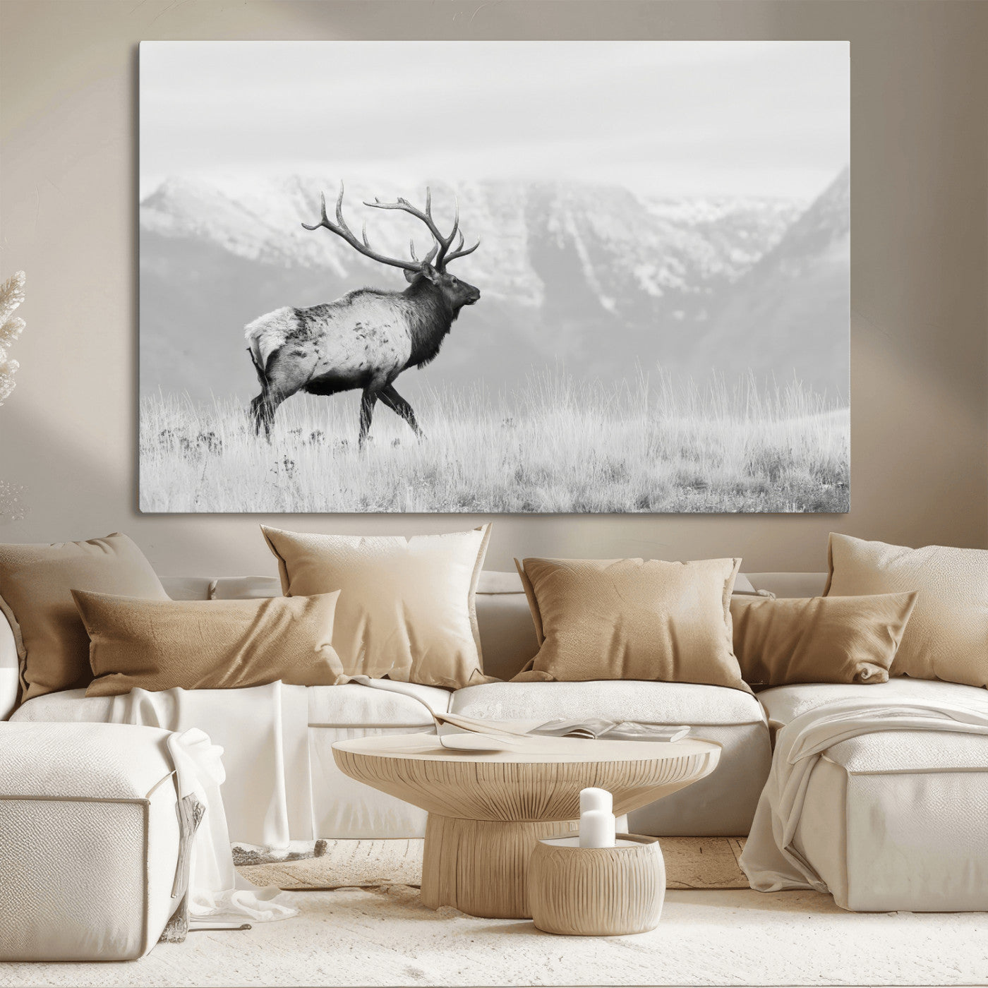 Black and white photograph of a majestic elk standing in a grassy field with snow-capped mountains in the background, creating a bold and rustic wilderness scene.