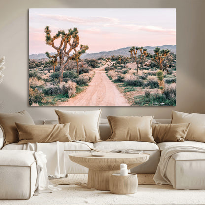 A dusty road winding through Joshua Tree National Park, framed by iconic twisted trees and warm desert tones under a soft pastel sky.