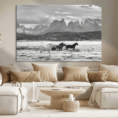 A black and white landscape of wild horses grazing in a vast grassland with towering mountains in the background, creating a moody and rustic western aesthetic.