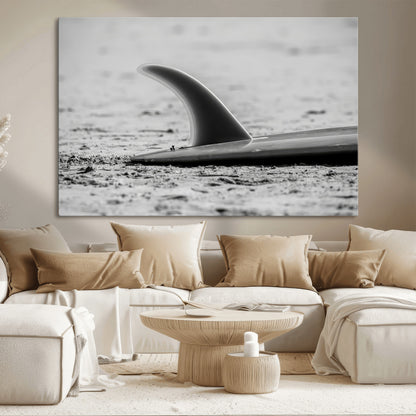 A black and white close-up of a surfboard fin resting on the sandy shore, highlighting minimalist beach aesthetics and classic surf culture.