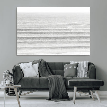 Monochrome photo of a lone surfer in calm layered waves, perfect for minimalist coastal or moody ocean-inspired wall decoration.