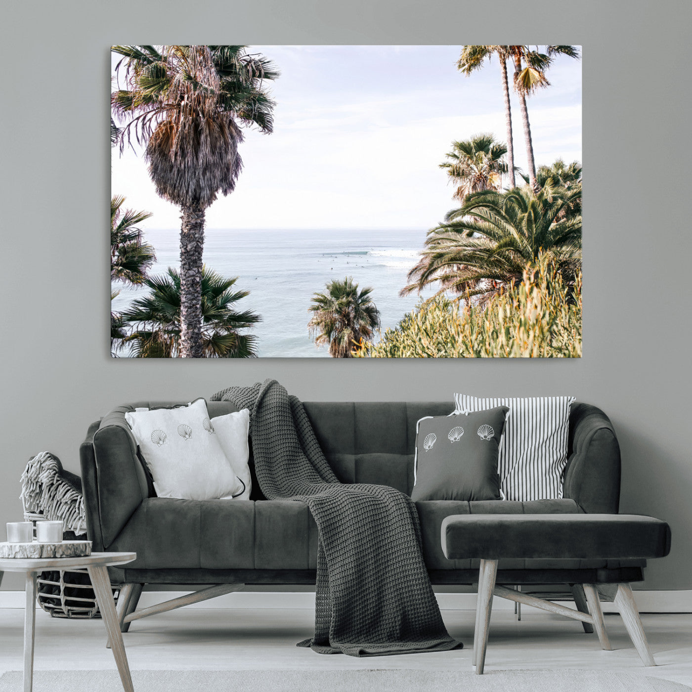 Scenic coastal view with tall palm trees overlooking a calm ocean, soft blue waves, and surfers in the distance, creating a peaceful tropical vibe.