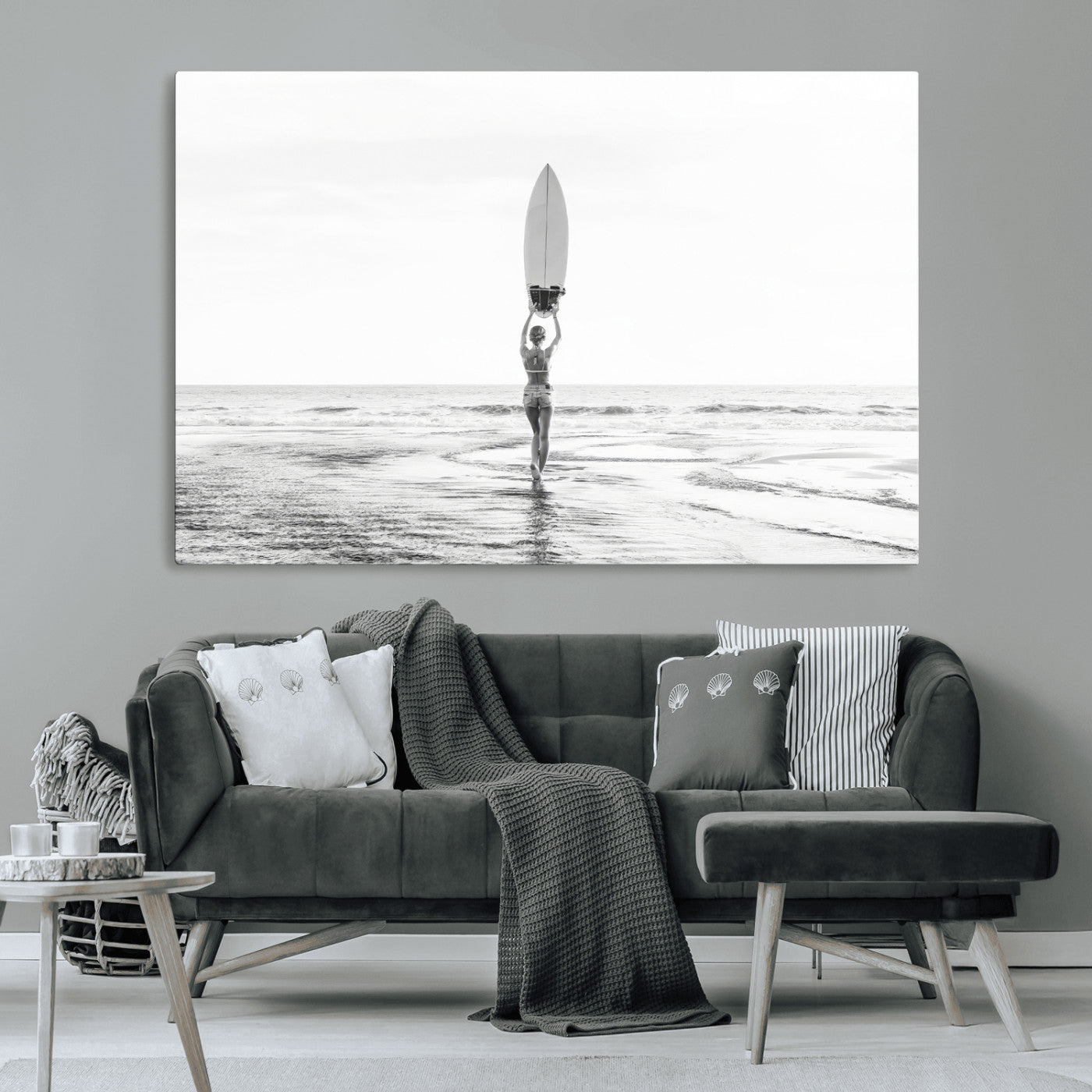 Black and white image of a female surfer holding a surfboard above her head while walking toward the ocean, creating a minimalist and bold coastal aesthetic.