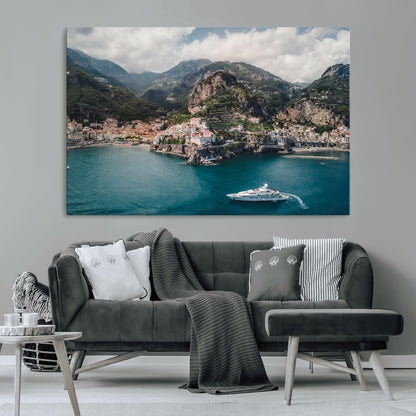 Aerial view of Amalfi Coast, Italy, with colorful hillside houses, lush green mountains, and a luxury yacht sailing in turquoise waters.