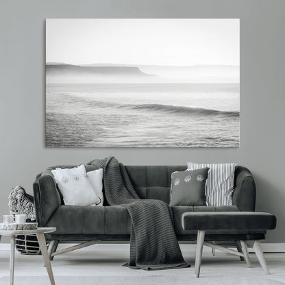 A black and white minimalist seascape featuring soft rolling waves and misty distant cliffs, creating a serene and timeless coastal atmosphere.