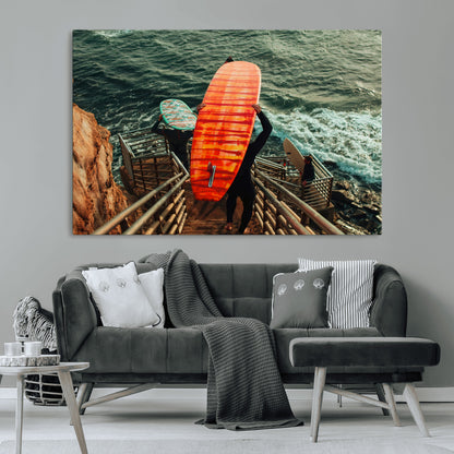 A surfer carrying a bold orange surfboard down a rugged staircase toward the ocean, bathed in golden hour light, capturing the energy of coastal adventure.
