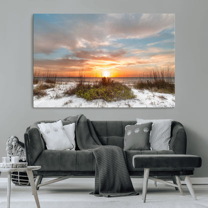 A tranquil beach scene featuring golden sunset hues over the water, with grasses in the foreground and a peaceful, serene atmosphere.