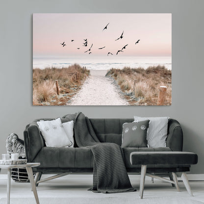 A peaceful coastal pathway leading to the ocean, with birds flying across a soft pastel sky, creating a calm and scenic beach atmosphere.