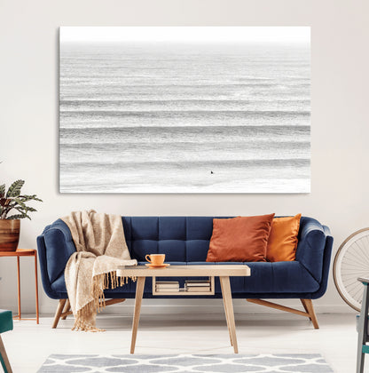 Monochrome photo of a lone surfer in calm layered waves, perfect for minimalist coastal or moody ocean-inspired wall decoration.