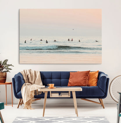 Dreamy photo of surfers waiting on soft pastel waves under a pink sunset sky, ideal for soft coastal minimalist or serene ocean-themed home decor.