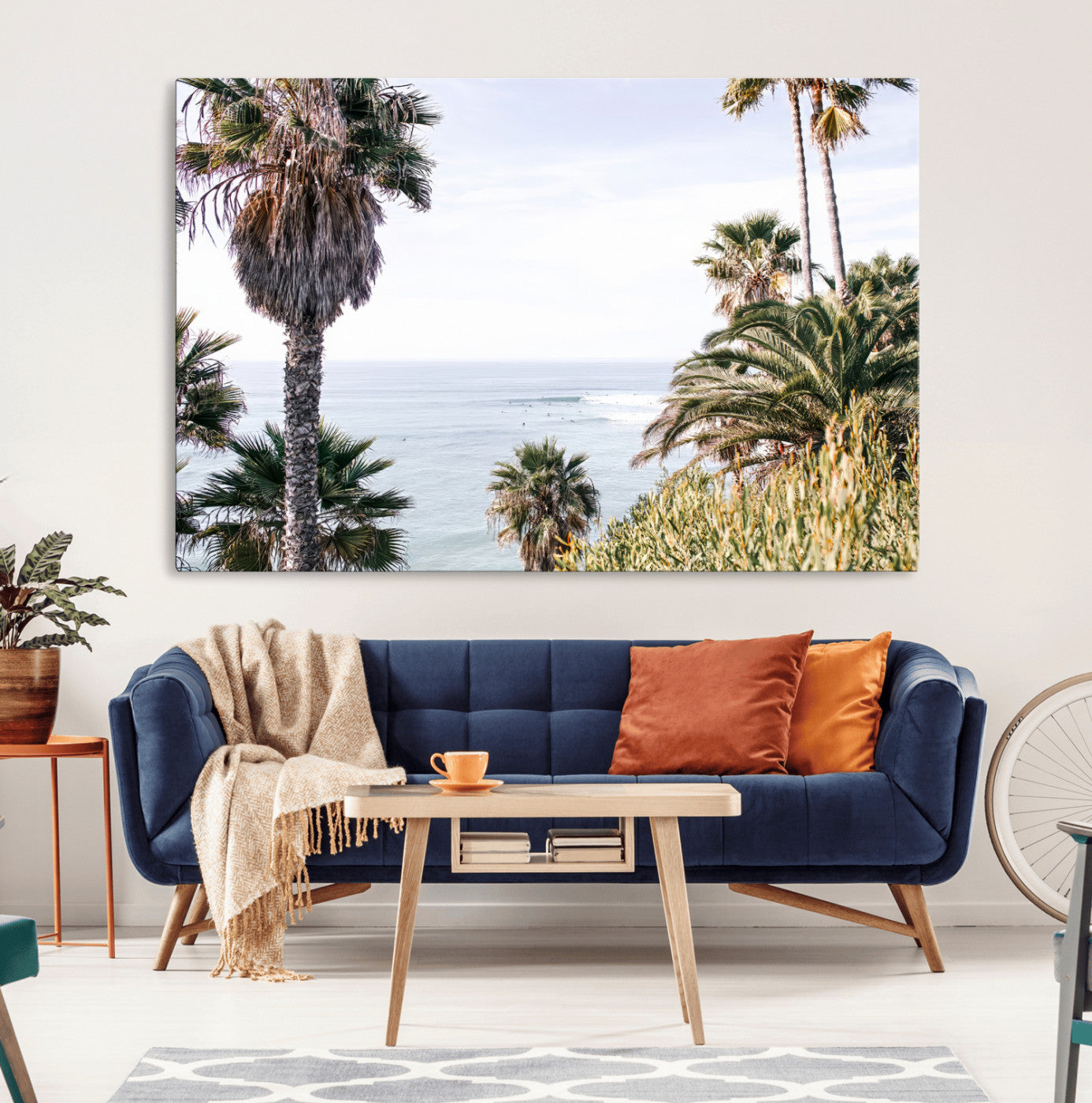 Scenic coastal view with tall palm trees overlooking a calm ocean, soft blue waves, and surfers in the distance, creating a peaceful tropical vibe.