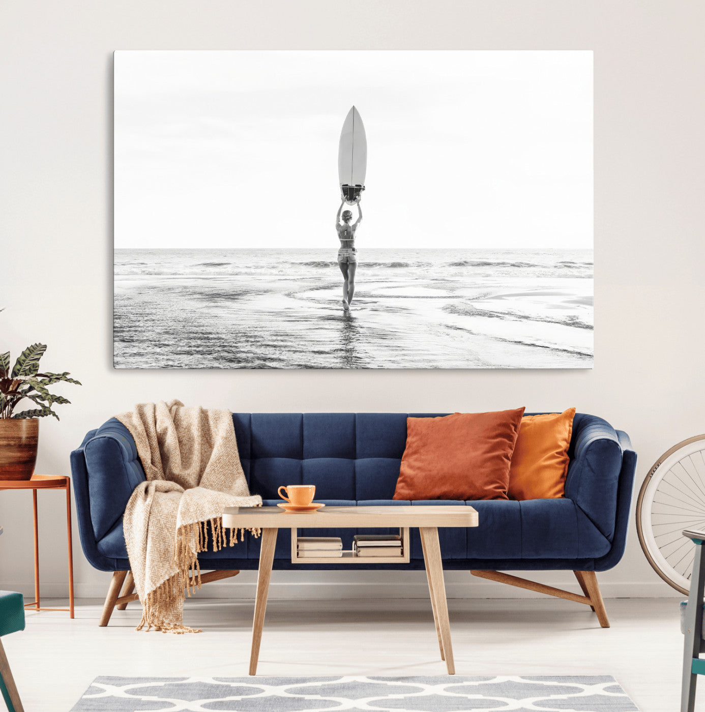 Black and white image of a female surfer holding a surfboard above her head while walking toward the ocean, creating a minimalist and bold coastal aesthetic.