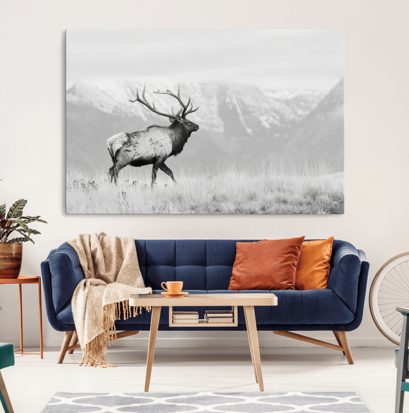 Black and white photograph of a majestic elk standing in a grassy field with snow-capped mountains in the background, creating a bold and rustic wilderness scene.