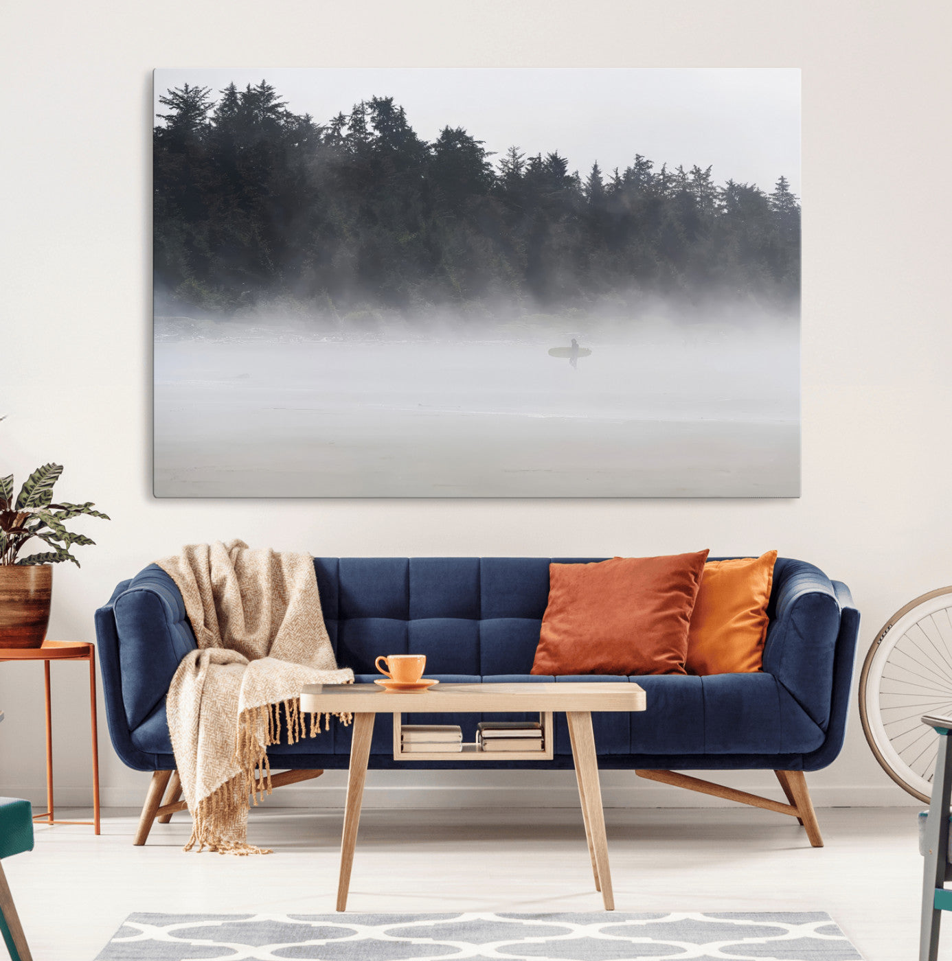 A lone surfer carrying a board through a misty shoreline, surrounded by dense trees and fog, creating a peaceful and mysterious coastal scene.