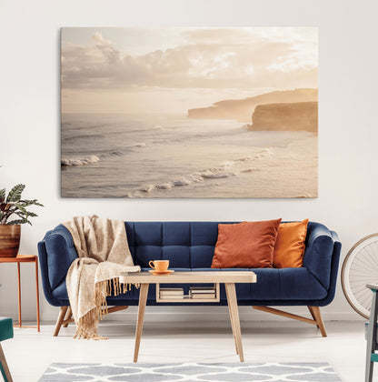 Golden hour seascape with misty cliffs and gentle waves rolling towards the shore, capturing a tranquil and warm coastal atmosphere.