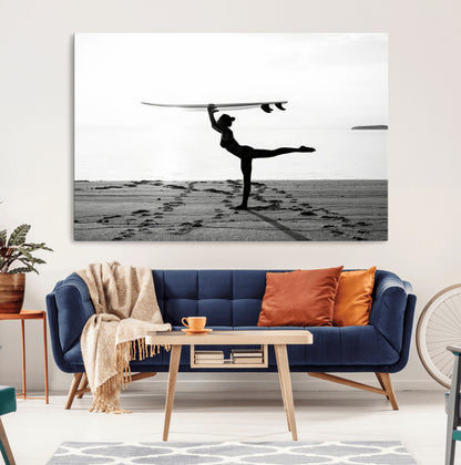 A woman balances a surfboard on her head while striking a yoga pose on the beach, silhouetted against a calm ocean horizon.