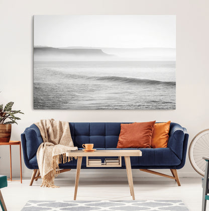A black and white minimalist seascape featuring soft rolling waves and misty distant cliffs, creating a serene and timeless coastal atmosphere.