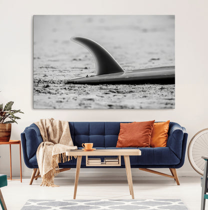 A black and white close-up of a surfboard fin resting on the sandy shore, highlighting minimalist beach aesthetics and classic surf culture.