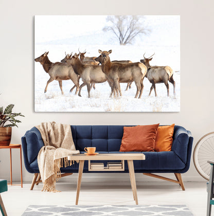 A group of elk standing on snowy terrain with a tree in the background, perfect for rustic or lodge-style winter wall decor.