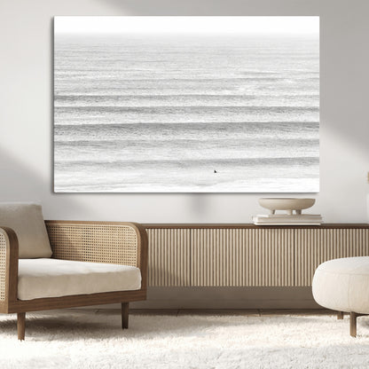 Monochrome photo of a lone surfer in calm layered waves, perfect for minimalist coastal or moody ocean-inspired wall decoration.