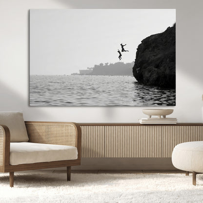Black and white canvas of two figures cliff jumping into the sea, captured with moody tones, ideal for modern coastal or adventure-themed home decor.   2/2