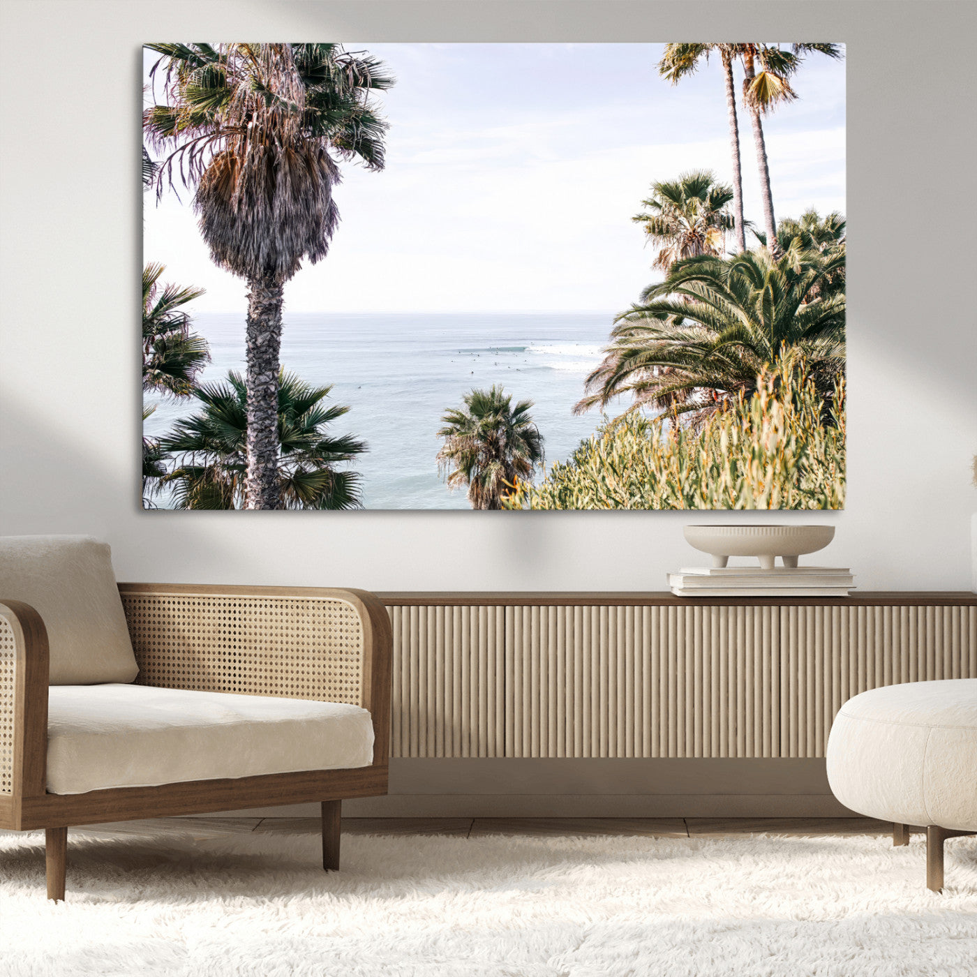 Scenic coastal view with tall palm trees overlooking a calm ocean, soft blue waves, and surfers in the distance, creating a peaceful tropical vibe.