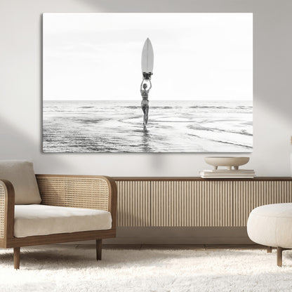 Black and white image of a female surfer holding a surfboard above her head while walking toward the ocean, creating a minimalist and bold coastal aesthetic.