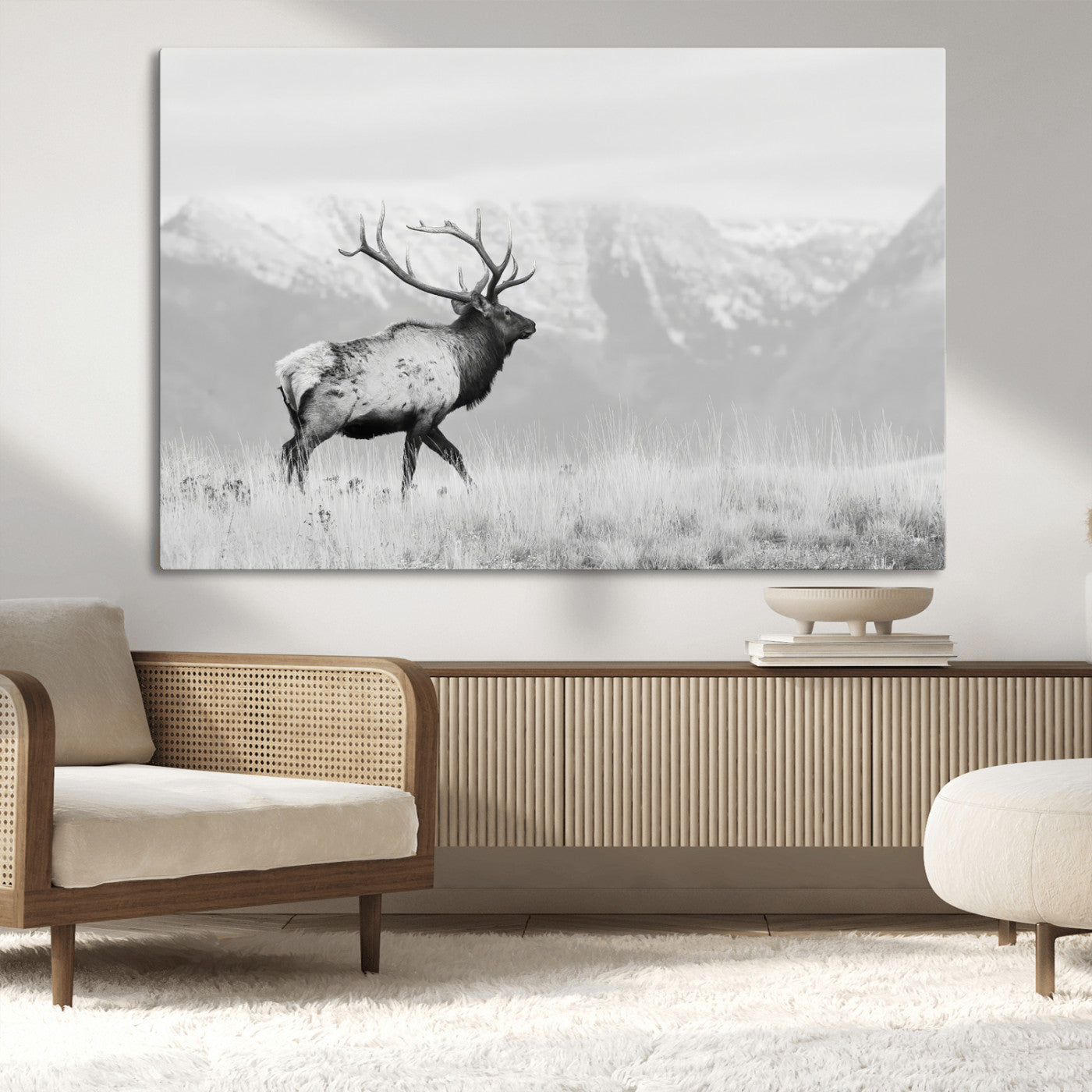 Black and white photograph of a majestic elk standing in a grassy field with snow-capped mountains in the background, creating a bold and rustic wilderness scene.