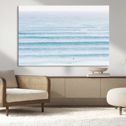 Minimalist ocean view with soft blue waves and a lone surfer, creating a serene and airy coastal aesthetic, perfect for tranquil home decor.