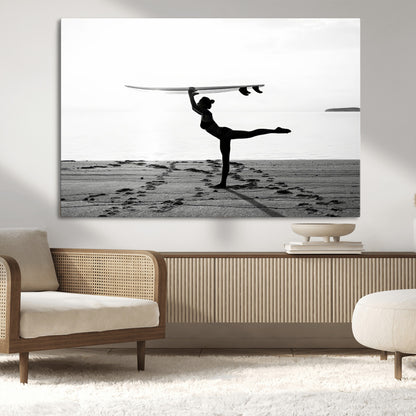 A woman balances a surfboard on her head while striking a yoga pose on the beach, silhouetted against a calm ocean horizon.