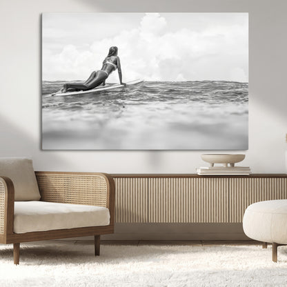 A black and white ocean scene featuring a surfer girl waiting on her board, gazing at the horizon, capturing a tranquil and adventurous coastal moment.