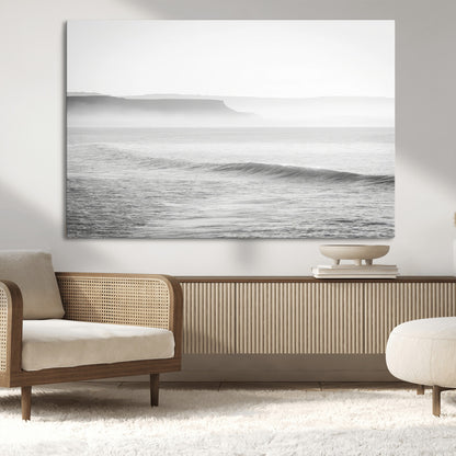 A black and white minimalist seascape featuring soft rolling waves and misty distant cliffs, creating a serene and timeless coastal atmosphere.
