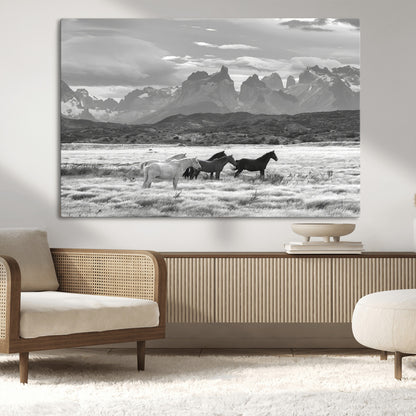 A black and white landscape of wild horses grazing in a vast grassland with towering mountains in the background, creating a moody and rustic western aesthetic.