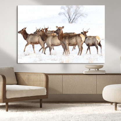 A group of elk standing on snowy terrain with a tree in the background, perfect for rustic or lodge-style winter wall decor.