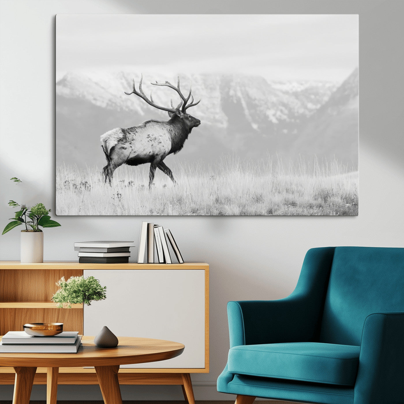 Black and white photograph of a majestic elk standing in a grassy field with snow-capped mountains in the background, creating a bold and rustic wilderness scene.
