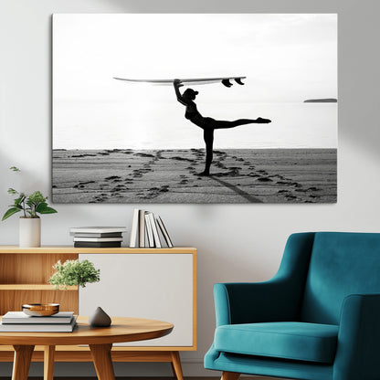 A woman balances a surfboard on her head while striking a yoga pose on the beach, silhouetted against a calm ocean horizon.