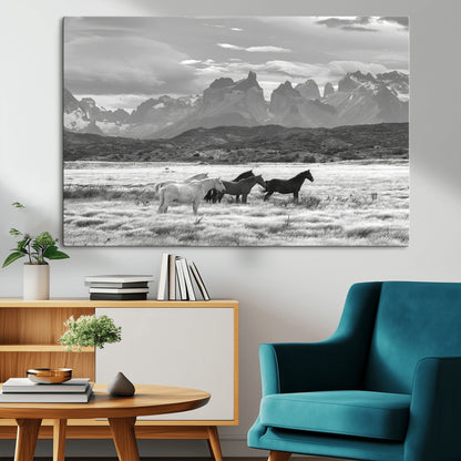 A black and white landscape of wild horses grazing in a vast grassland with towering mountains in the background, creating a moody and rustic western aesthetic.
