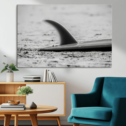 A black and white close-up of a surfboard fin resting on the sandy shore, highlighting minimalist beach aesthetics and classic surf culture.