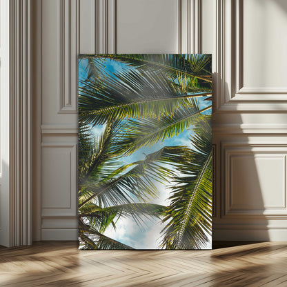 Looking up at lush green palm leaves against a bright blue sky, creating a tropical and relaxing coastal aesthetic.