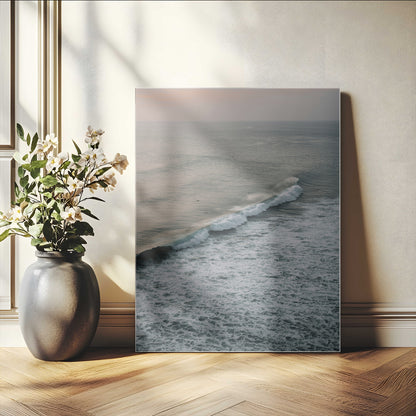 Aerial view of ocean waves rolling towards the shore under a soft sunset sky, creating a peaceful and minimalist coastal scene.