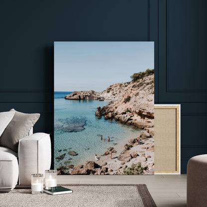 A vibrant coastal photo of a rocky Mediterranean cove with turquoise waters and beachgoers, ideal for boho coastal or summer-inspired interiors.