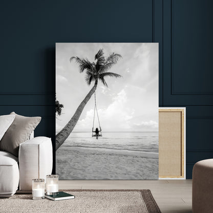 Monochrome photo of a woman swinging from a palm tree on a serene beach, ideal for minimalist or tropical coastal decor.
