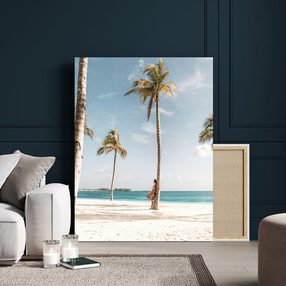 Person leaning on a palm tree at a tropical beach with white sand and turquoise water, perfect for coastal or beach-themed home decor.