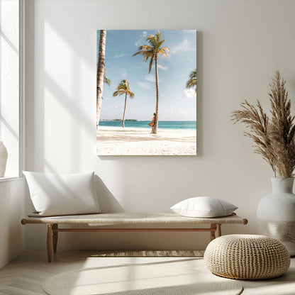 Person leaning on a palm tree at a tropical beach with white sand and turquoise water, perfect for coastal or beach-themed home decor.