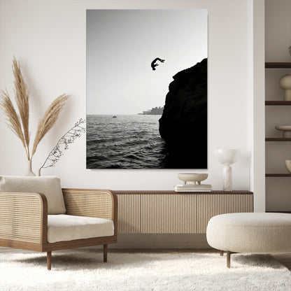 Silhouette of a person mid-air during a cliff jump over the ocean, captured in black and white for minimalist adventure decor.